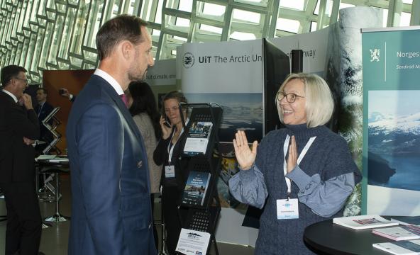 Førsteammanuensis Elena Dybtsyna gestikulerer og snakker med Kronprins Haakon på en stand under konferanse
