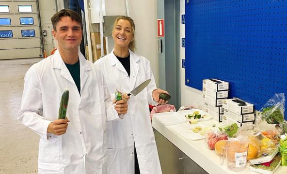 Mannlig og kvinnelig student i hvite dresser ved siden av frukt og grønt