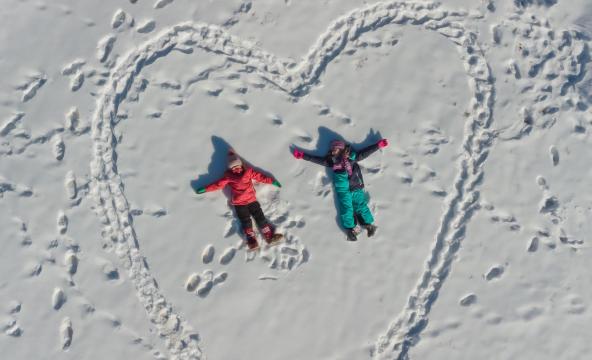 To barn som ligger i snøen sett fra lufta. Barna ligger inne i et stort opptråkka hjertemønster.