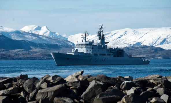 Kystvakten i en fjord på vinteren med snøkledte fjell bak. Foto