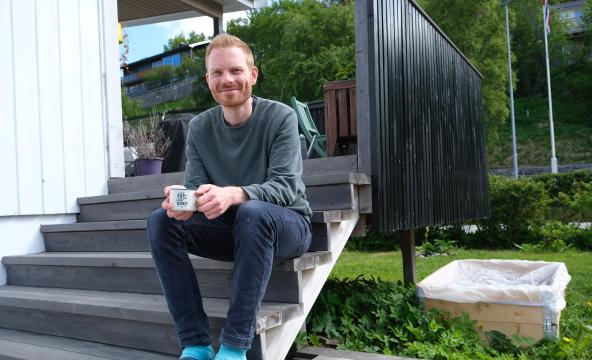 Mathias Reinar sitter på trappa utenfor hjemmet sitt med en kaffekopp i handa