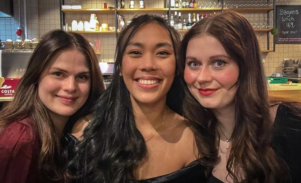 Tre unge kvinner som står tett i tett på en kafé. Foto