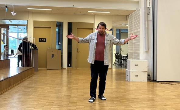 Mann slår ut med armene inne i et stort lokale.