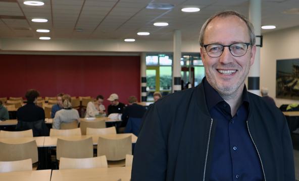 Mann i kantineområde, med folk bak. Veiledningsped. Veiledningspedagogikk. Foto