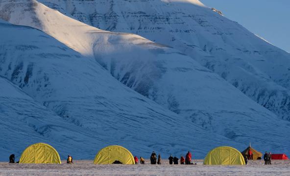 Arktisk fjell med teltleir på bakken ved fjellets fot. Foto