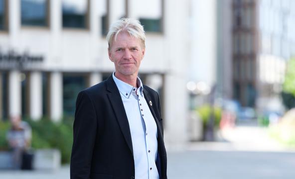 Smilende mann i dress foran bygning