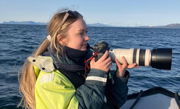 Ung kvinne i båt på havet med stort kamera. Foto
