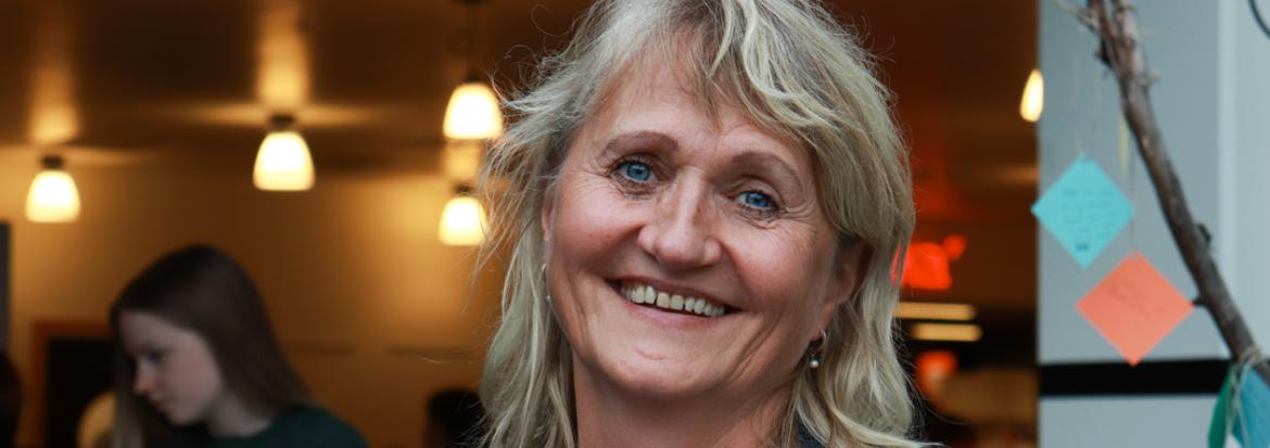 Kvinne som smiler og ser i kamera med folk i bakgrunnen