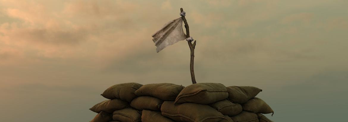 Hvitt flagg som vaier i luften fra en haug med sandsekker i en ørken