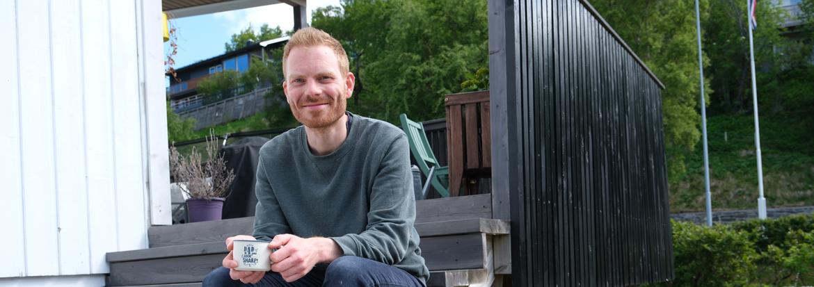 Mathias Reinar sitter på trappa utenfor hjemmet sitt med en kaffekopp i handa