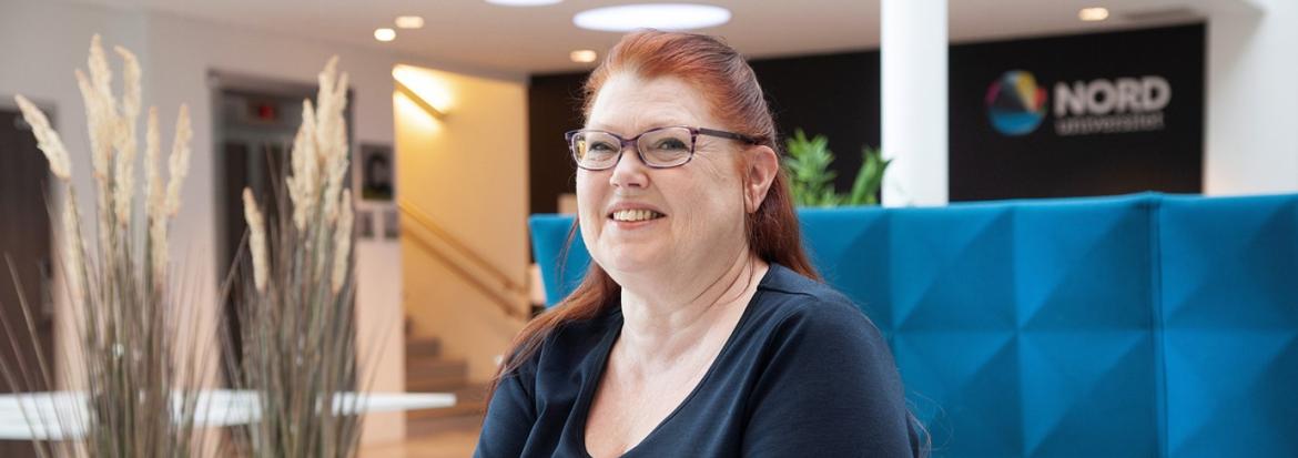 Kvinne med briller smiler i blå sofa