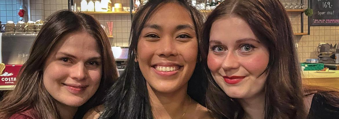 Tre unge kvinner som står tett i tett på en kafé. Foto