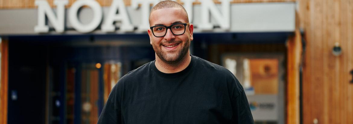 Ung mann med briller står foran bygg skiltet Noatun. Foto