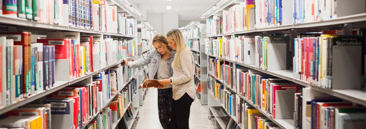 To unge damer ser på bøker i biblioteket