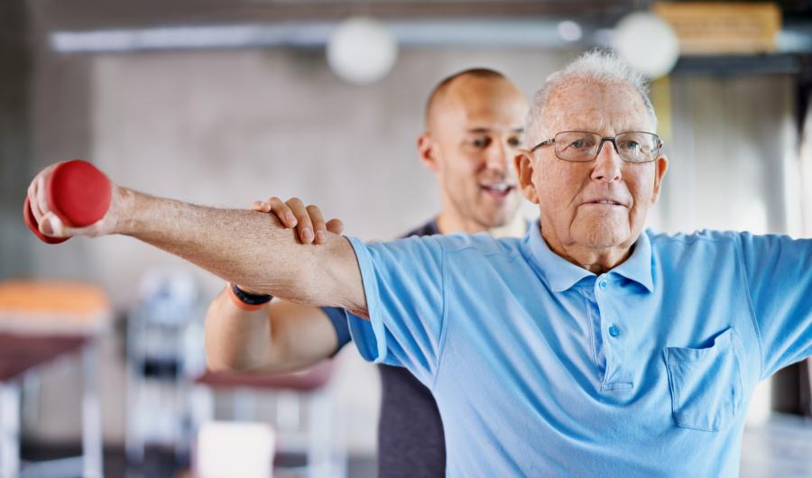 Eldre mann trener med vekter sammen med fysioterapeut