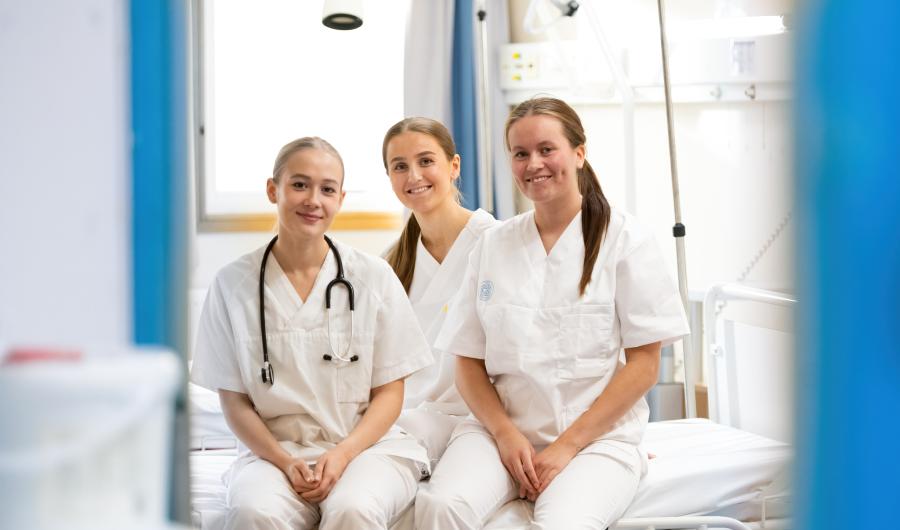 Tre sykepleiere som sitter på kanten av en sykeseng.