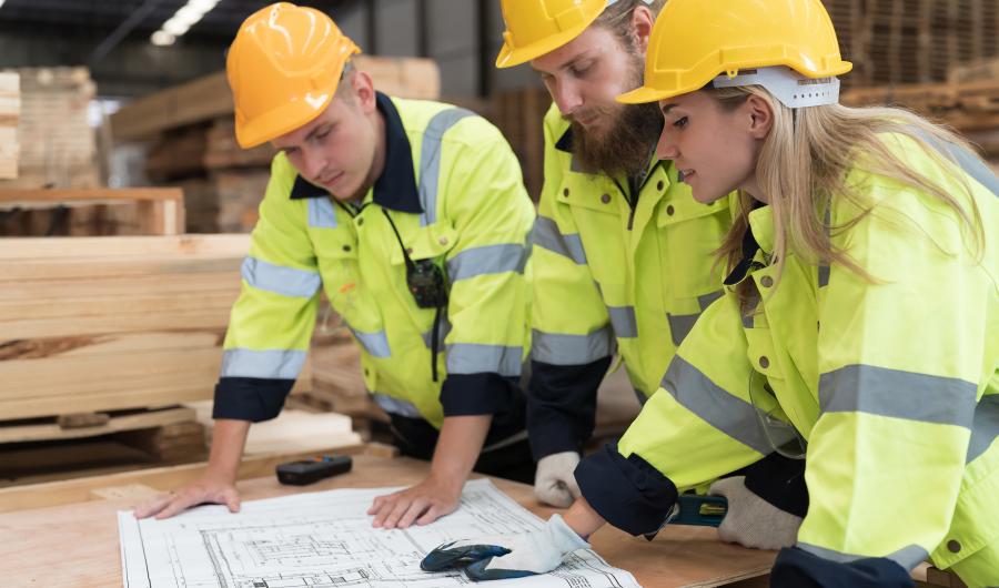 Tre personer i verneklær studerer en arbeidstegning.