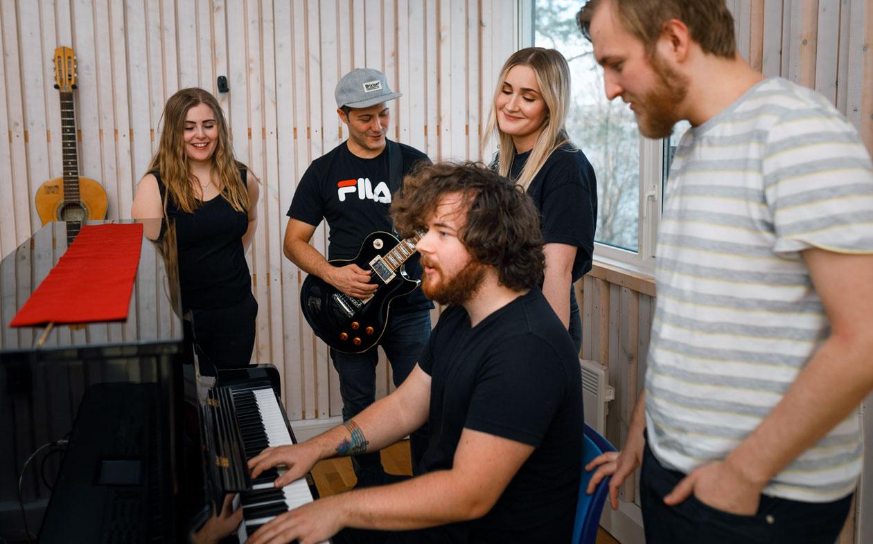 Fem musikkstudenter ved et piano.