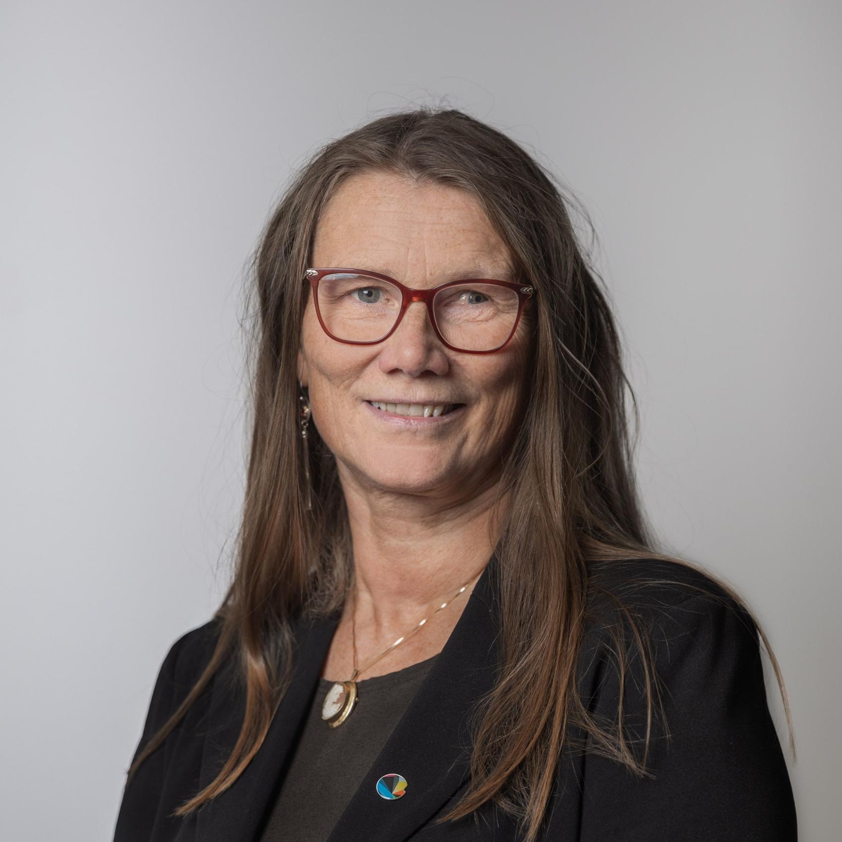 Smilende kvinne med brunt langt hår og svart jakke