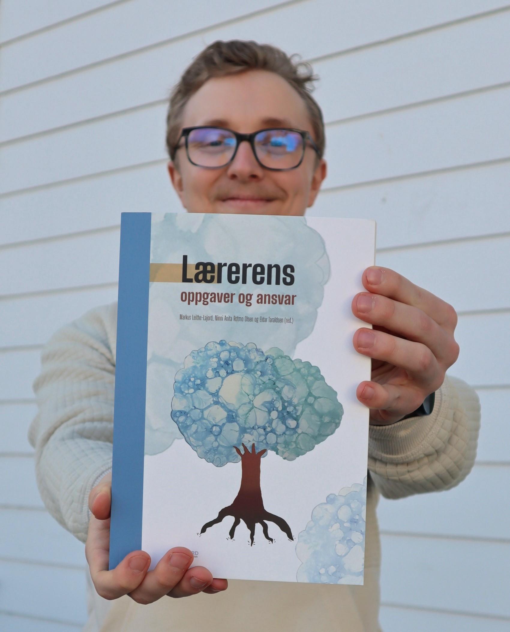 Mann med briller holder en bok fram mot kamera