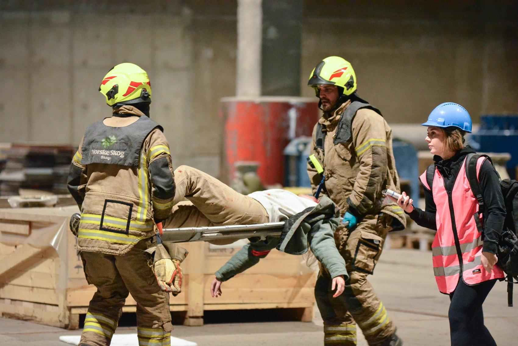 To redningsmenn med gule hjelmer bærer skadd person på båre