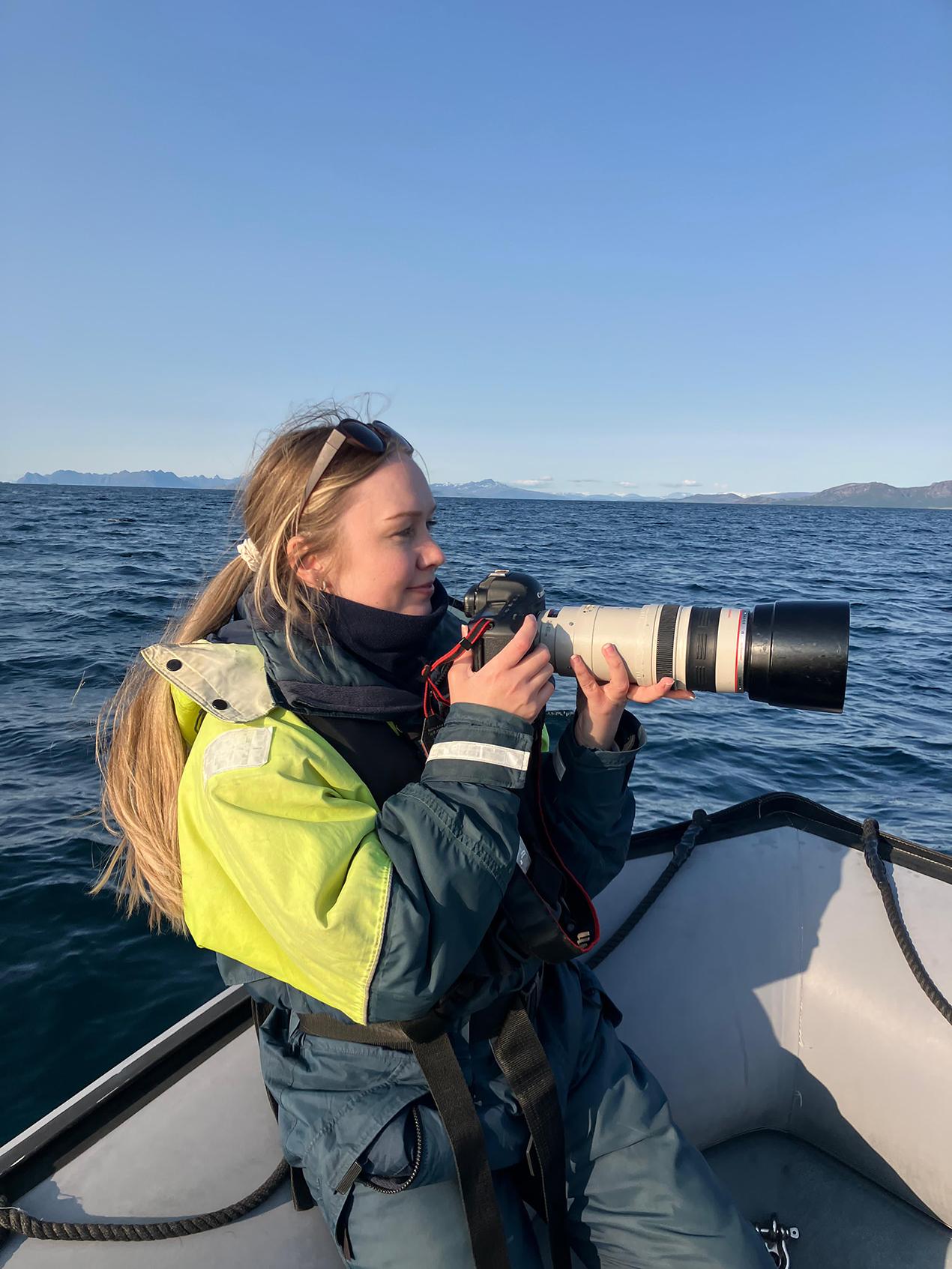 Kvinne med stort kamera i båt på havet. Foto