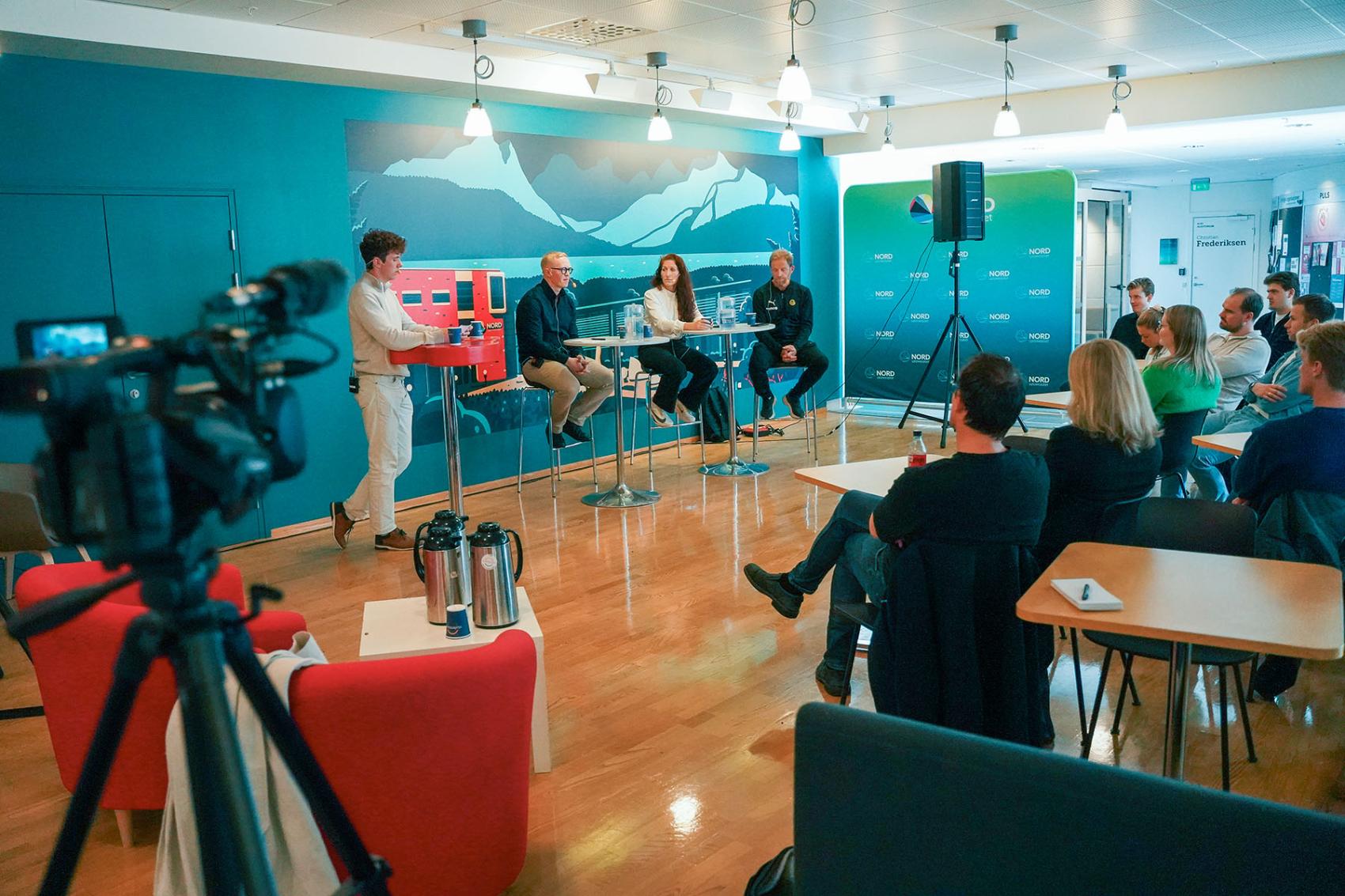 Bilde fra en debatt, med debattenter, kamera og publikum synlig.