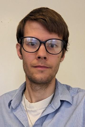 Mann med brunt hår, briller og ikledd blå skjorte