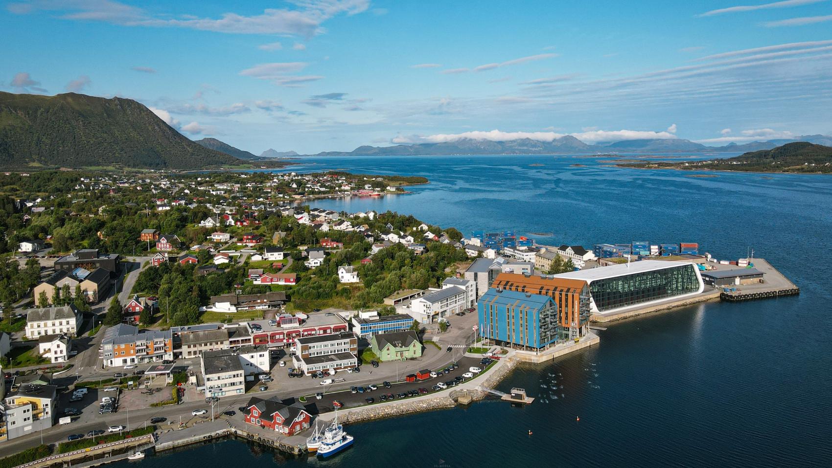 Bilde av et idyllisk tettsted på en fin sommersdag med fjorder og fjell i horisonten.