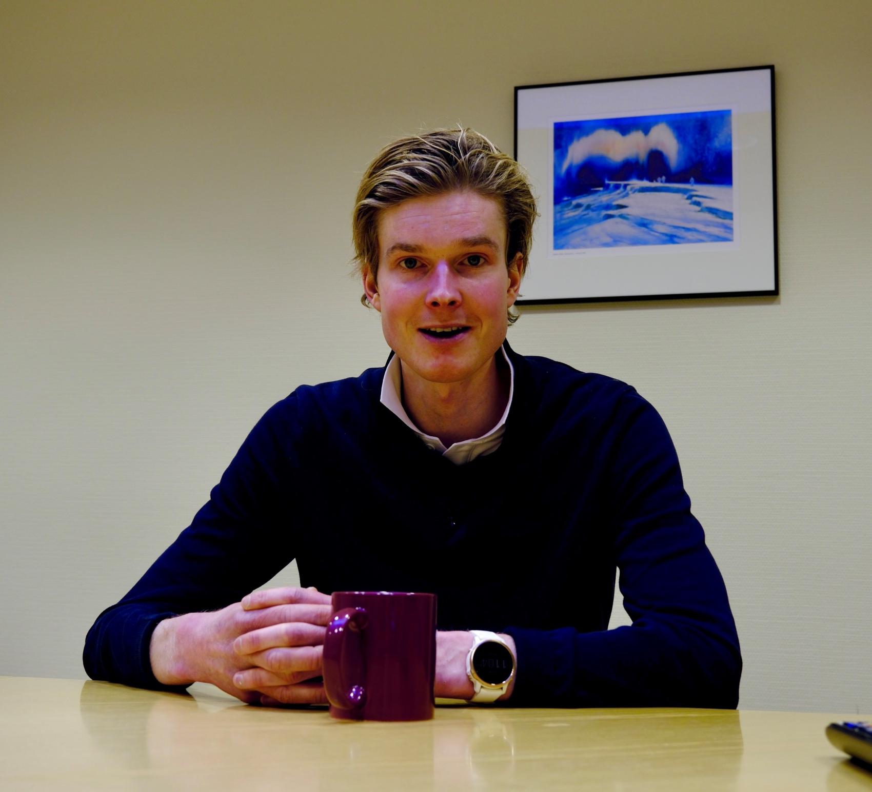 Ung mann ved bord med kaffekopp. Foto