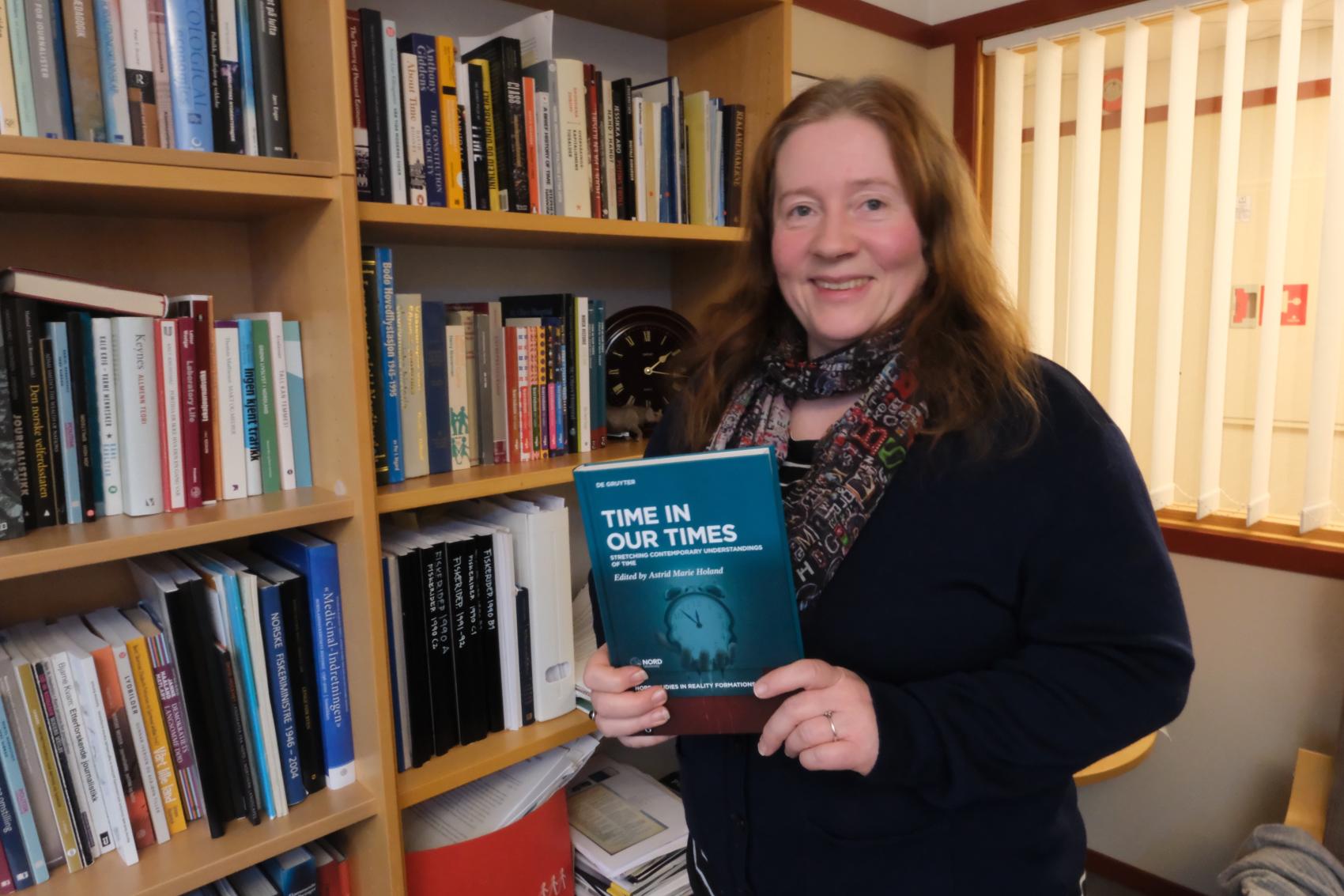 Dame ved bokhylle som holder i en bok. Foto