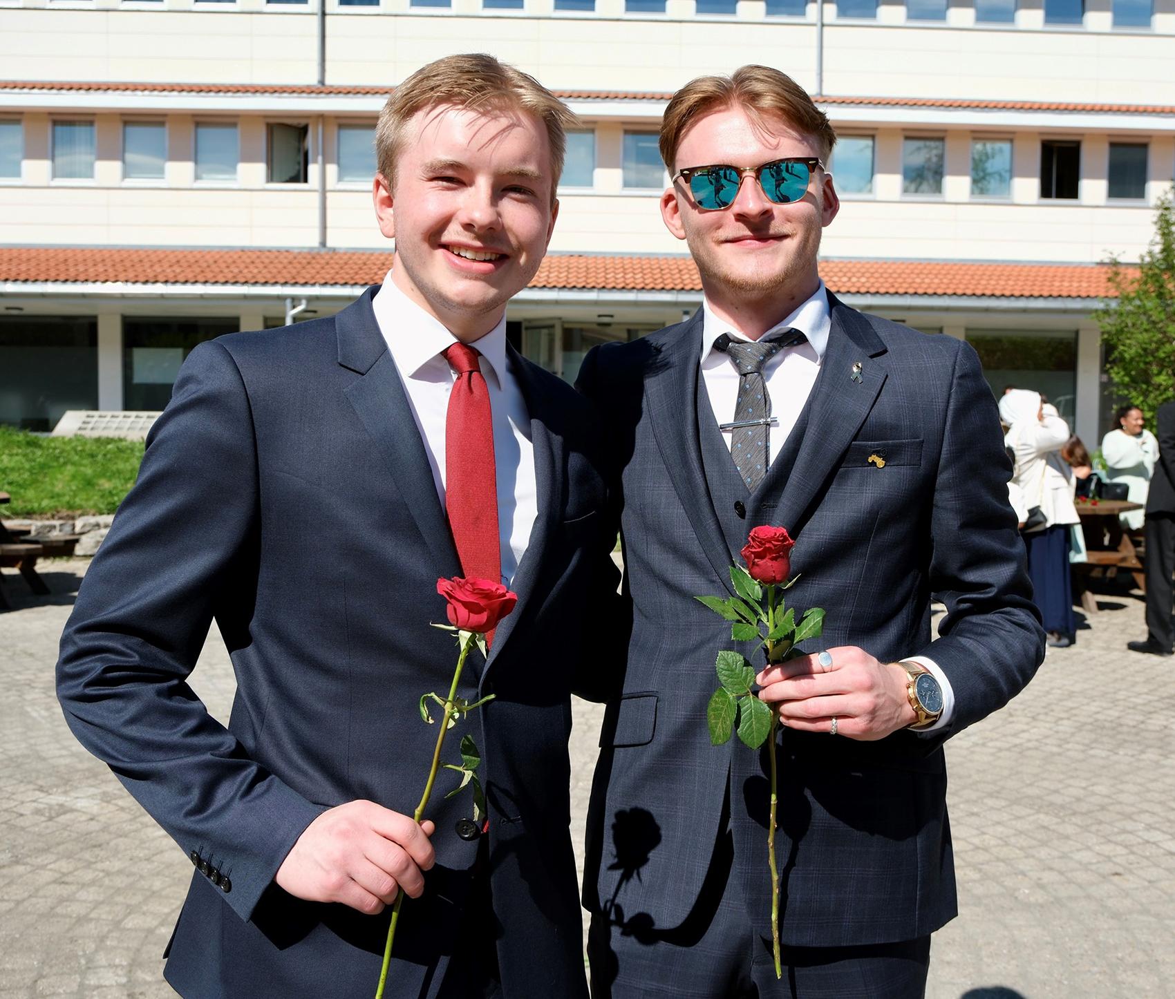 To dresskledde unge menn med rose i hånda. Foto