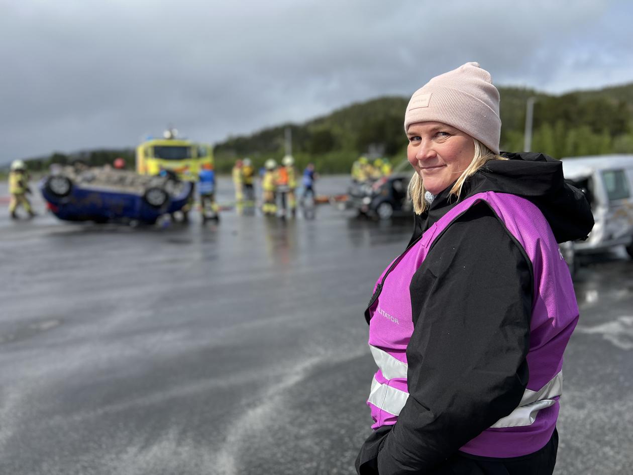 Kvinnelig øvingslærer på havaristed under øvelse med bilvrak og nødetater bak