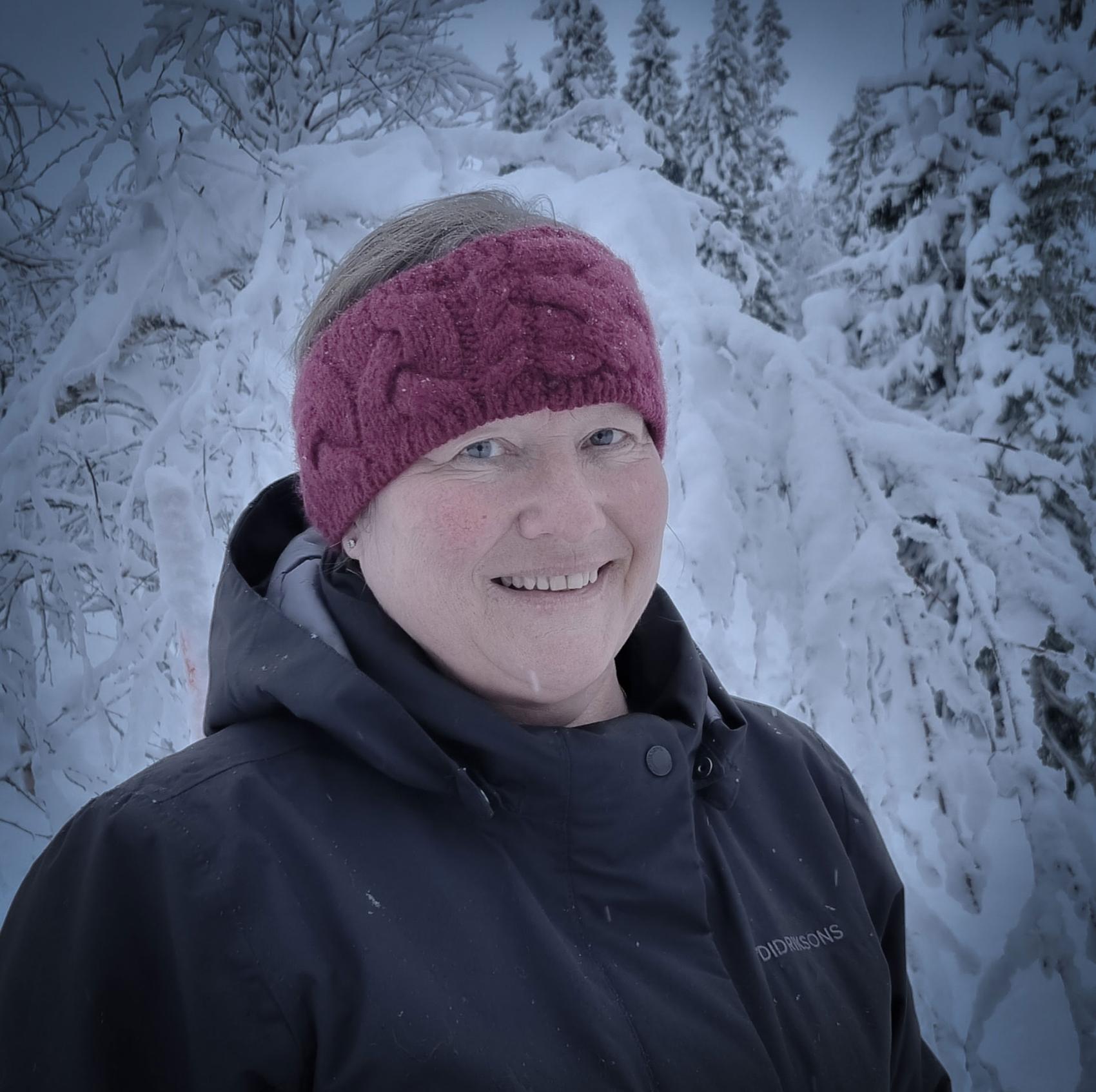 Nærbilde av en kvinne i vinterklær som står foran en snødekket skog 