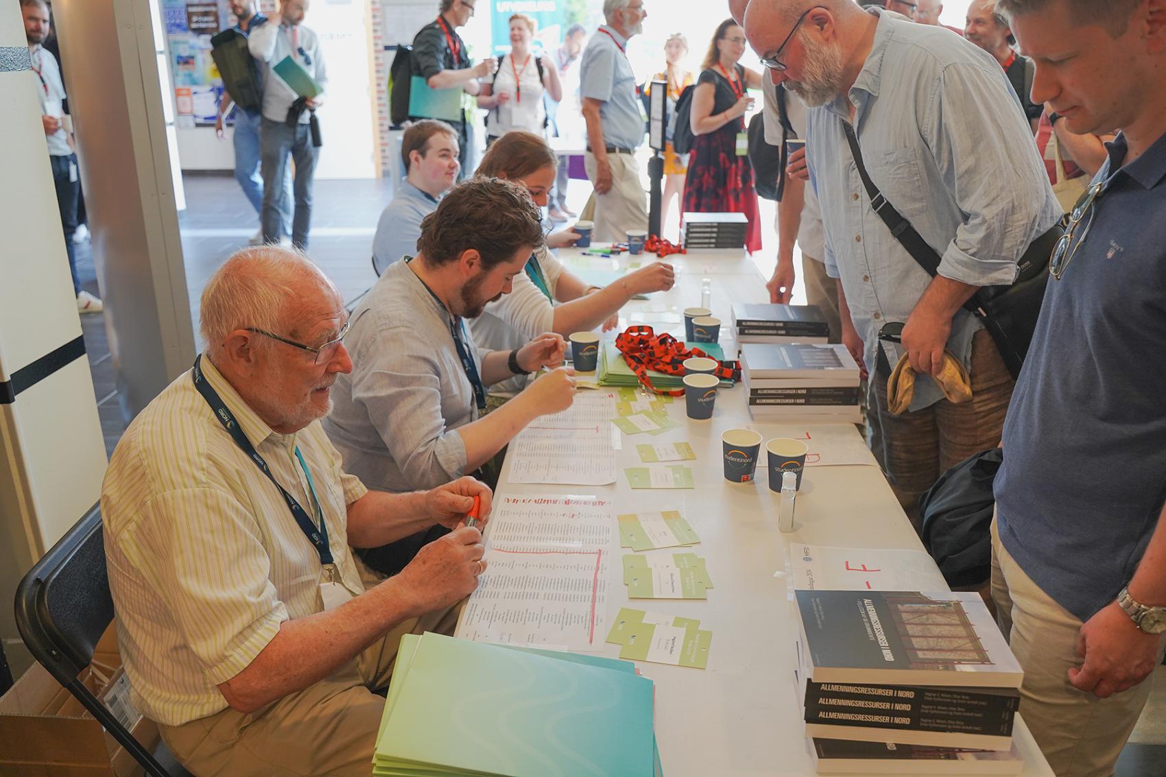 Mange menneske ved eit bord under konferanse. Foto