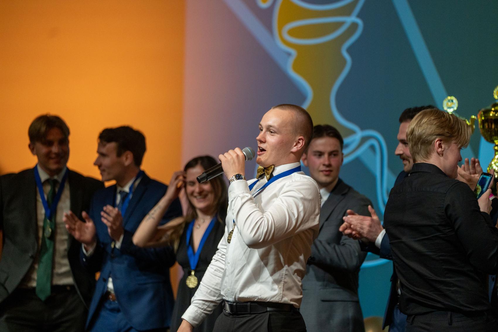 Mann i hvit skjorte på scene med mikrofon. Foto