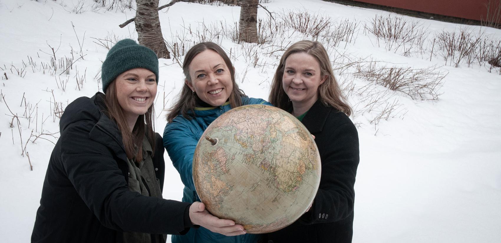 Tre kvinner som holder en globus, ute i vinterlandskap. Foto