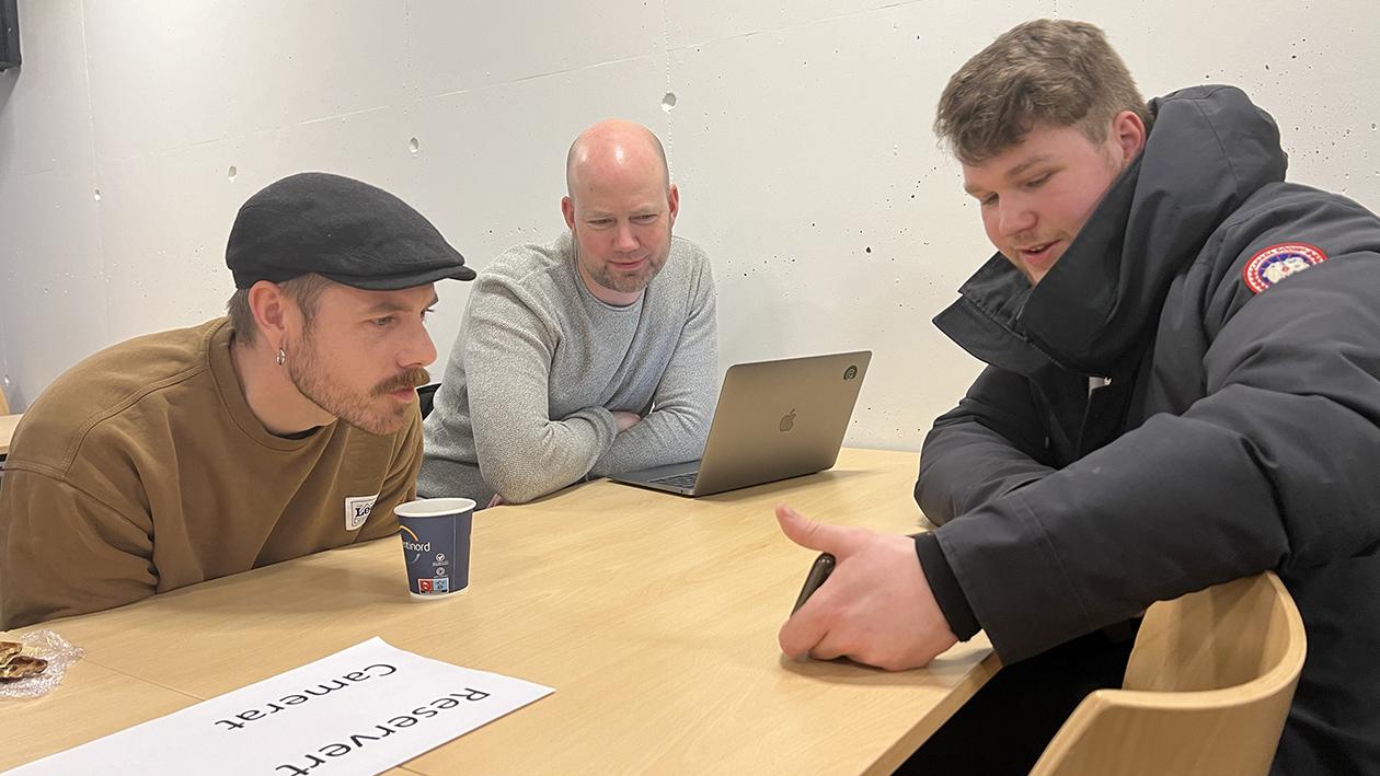 Tre menn ved ett bord med PC og smartphone. Foto