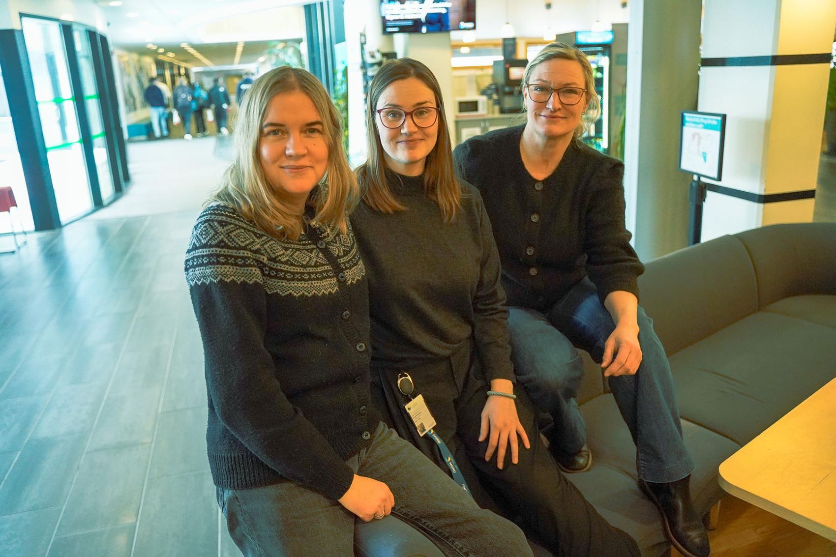 Tre kvinner i en sofa med mennesker i bakgrunn. Foto