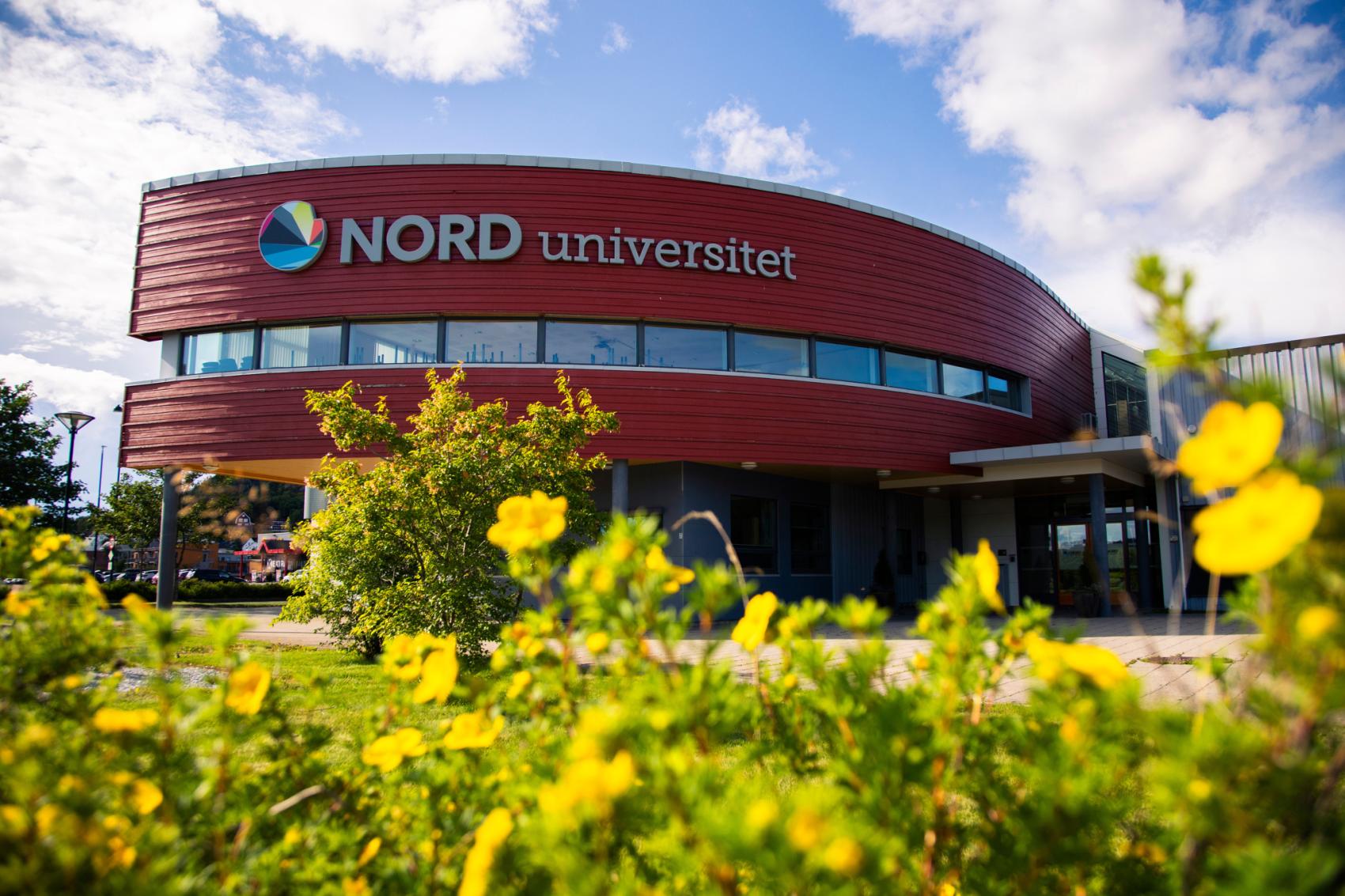 Fasade av universitetsbygg med blomster i front. Foto.