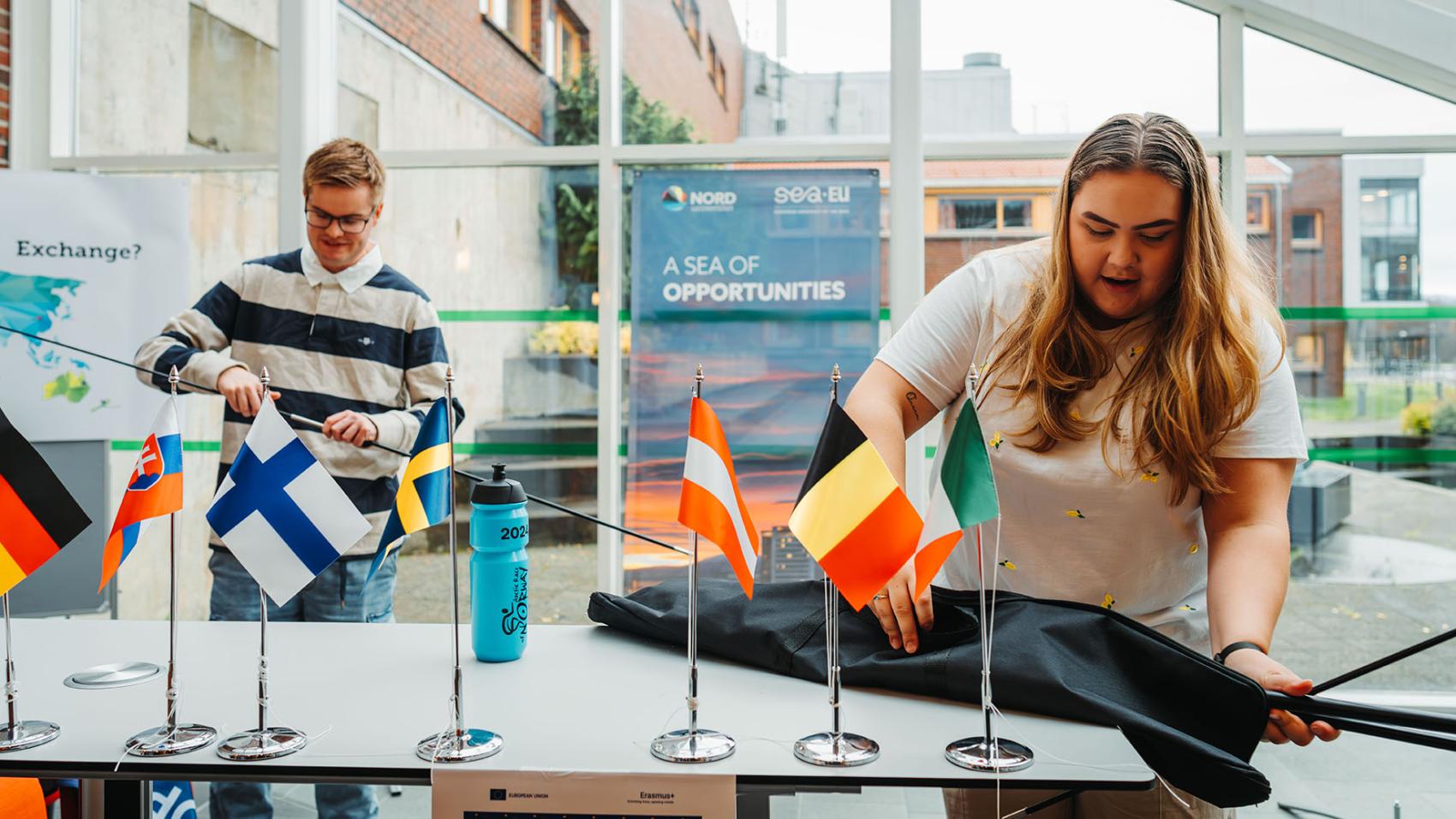 To unge studenter, mann og kvinne, som pynter en stand med ulike flagg. Foto