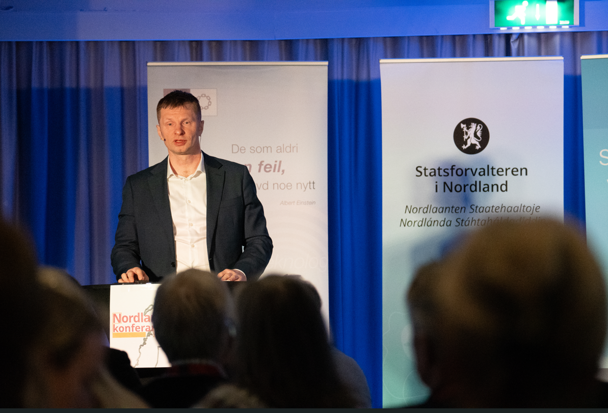 Mann som står og jholder en presentasjon foran forsamling. Foto