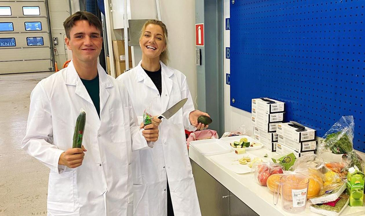 Mann og kvinne i hvite frakker ved bord med frukt og grønt