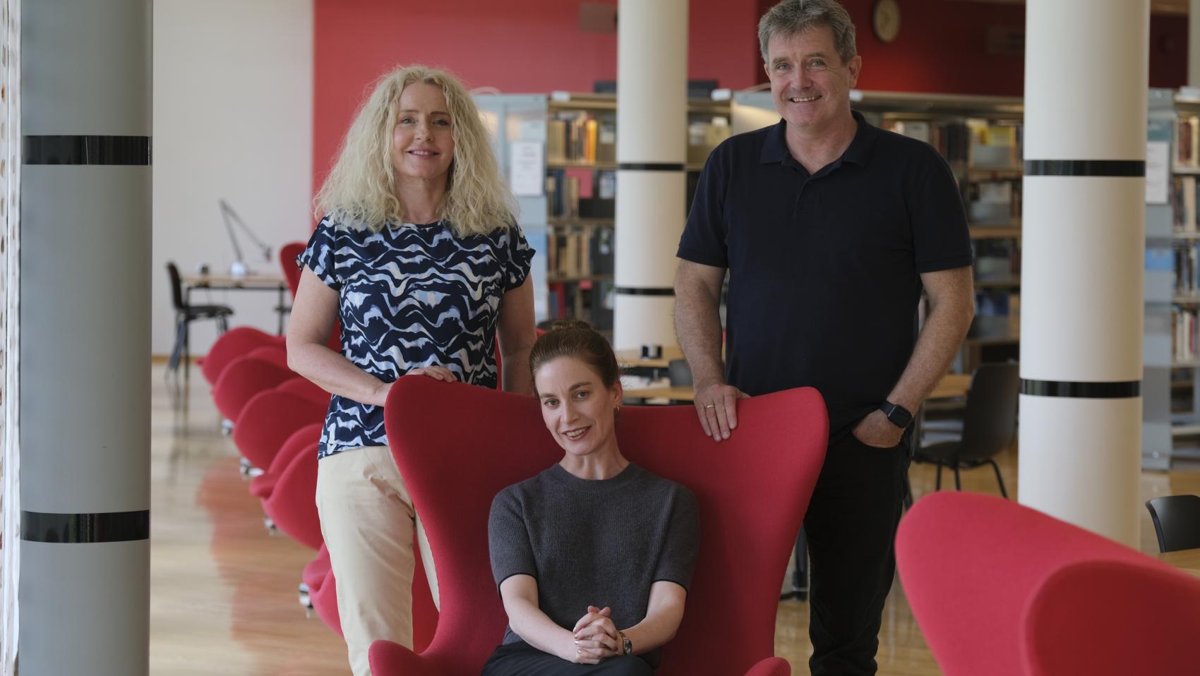 Tre mennesker i og bak en stol. Foto