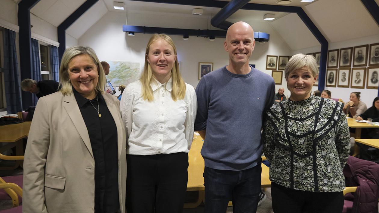 Fire personer som står i et lokale med mange mennesker i bakgrunn.