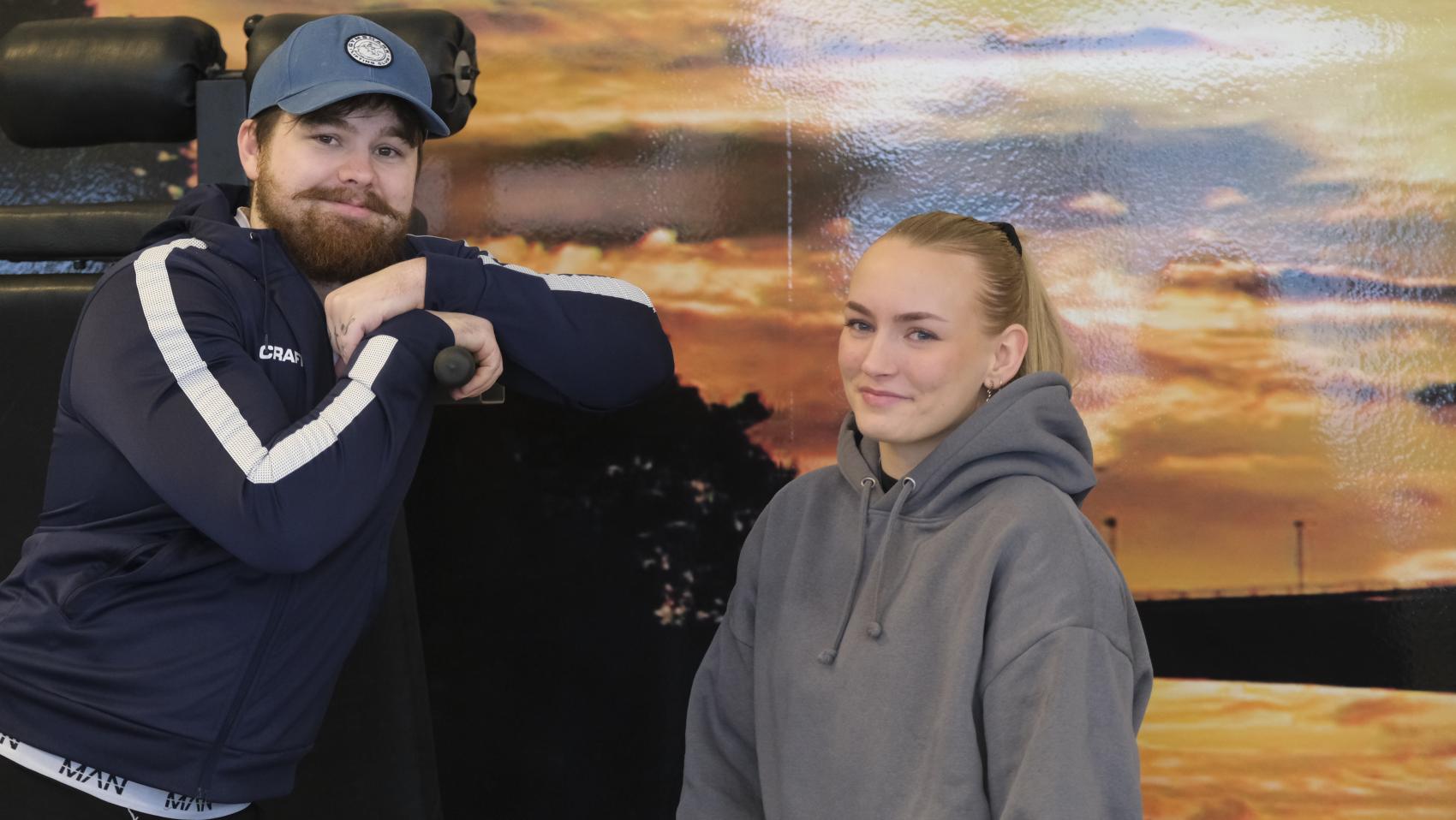 Ung mann med caps og ung kvinne ved treningsapparat. Foto