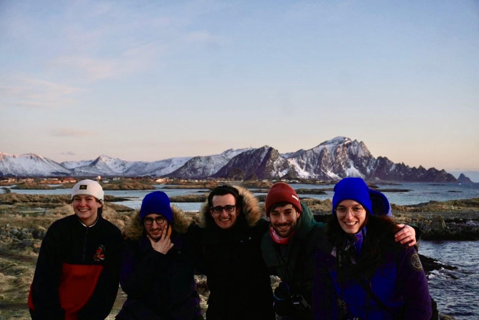 Fem unge mennesker ute foran landskap med spisse fjell og fjord.