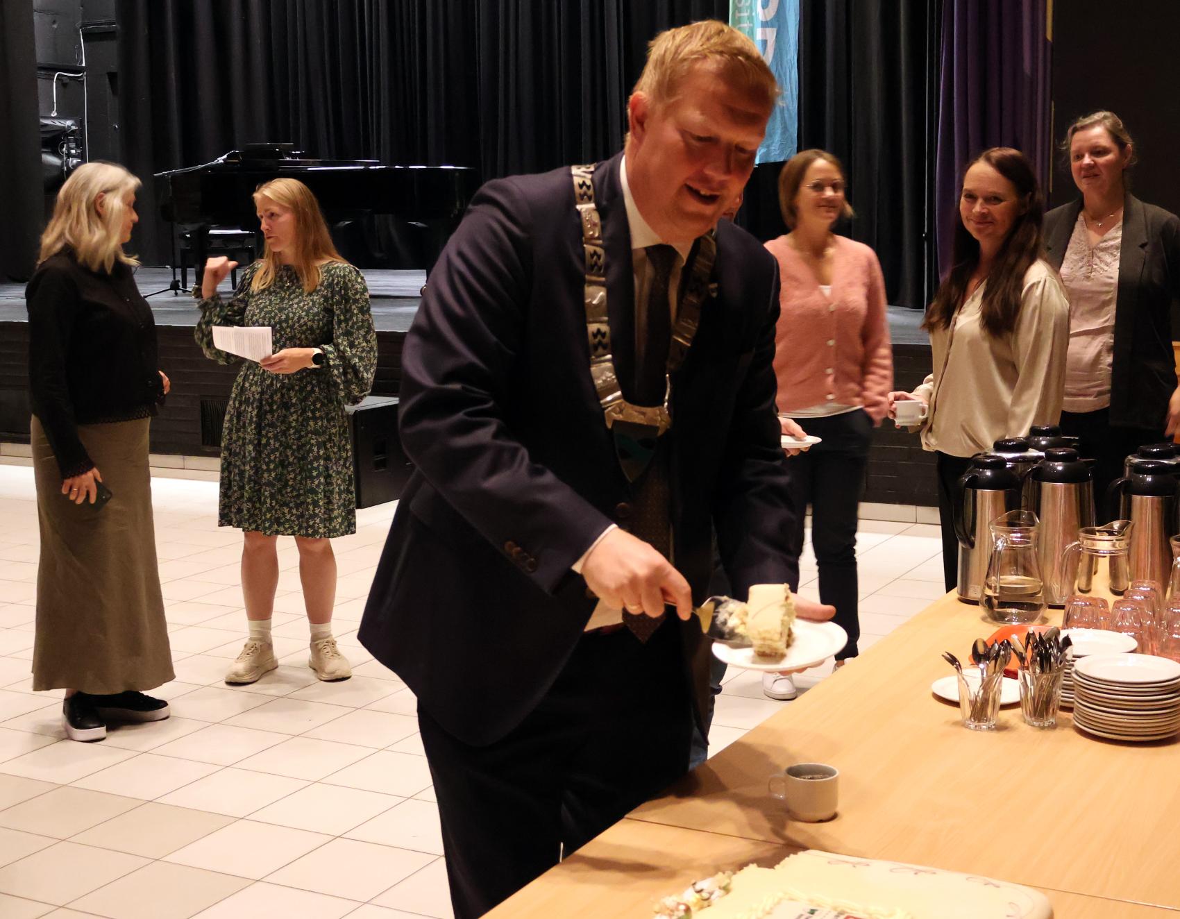 Mann i dress og med ordførerkjede forsyner seg av kake. Foto