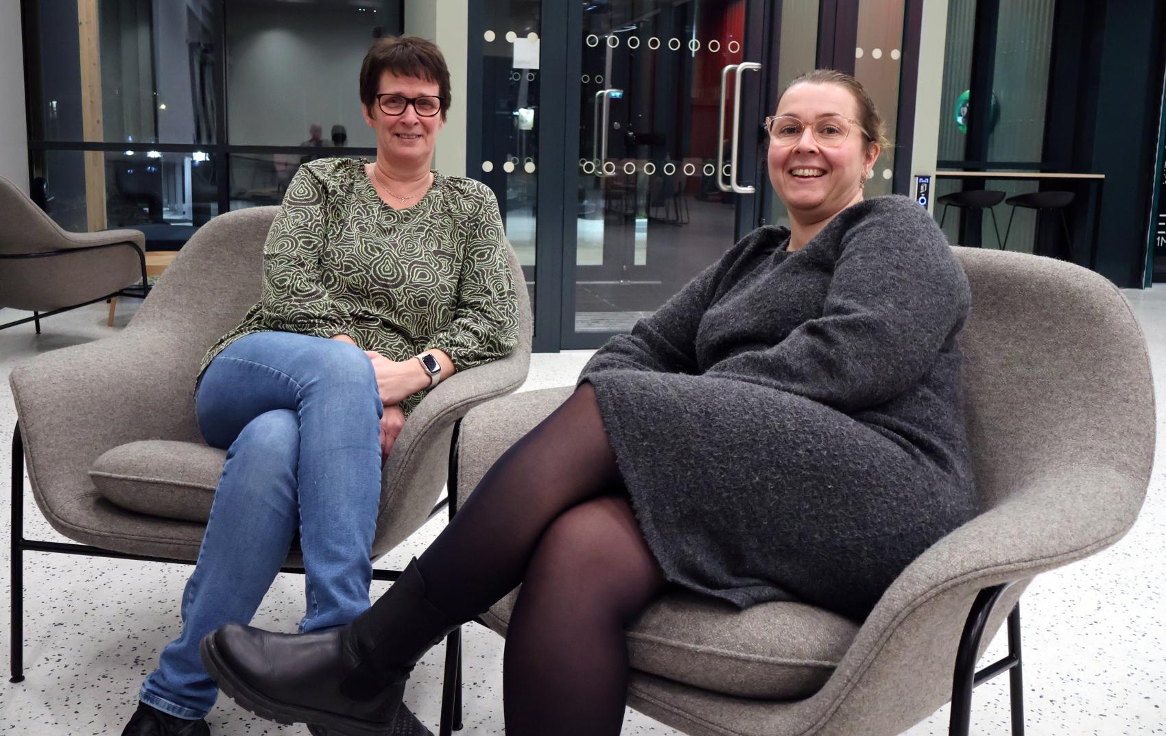 To kvinner som sitter i hver sin gogstol i en foaje på en skole.