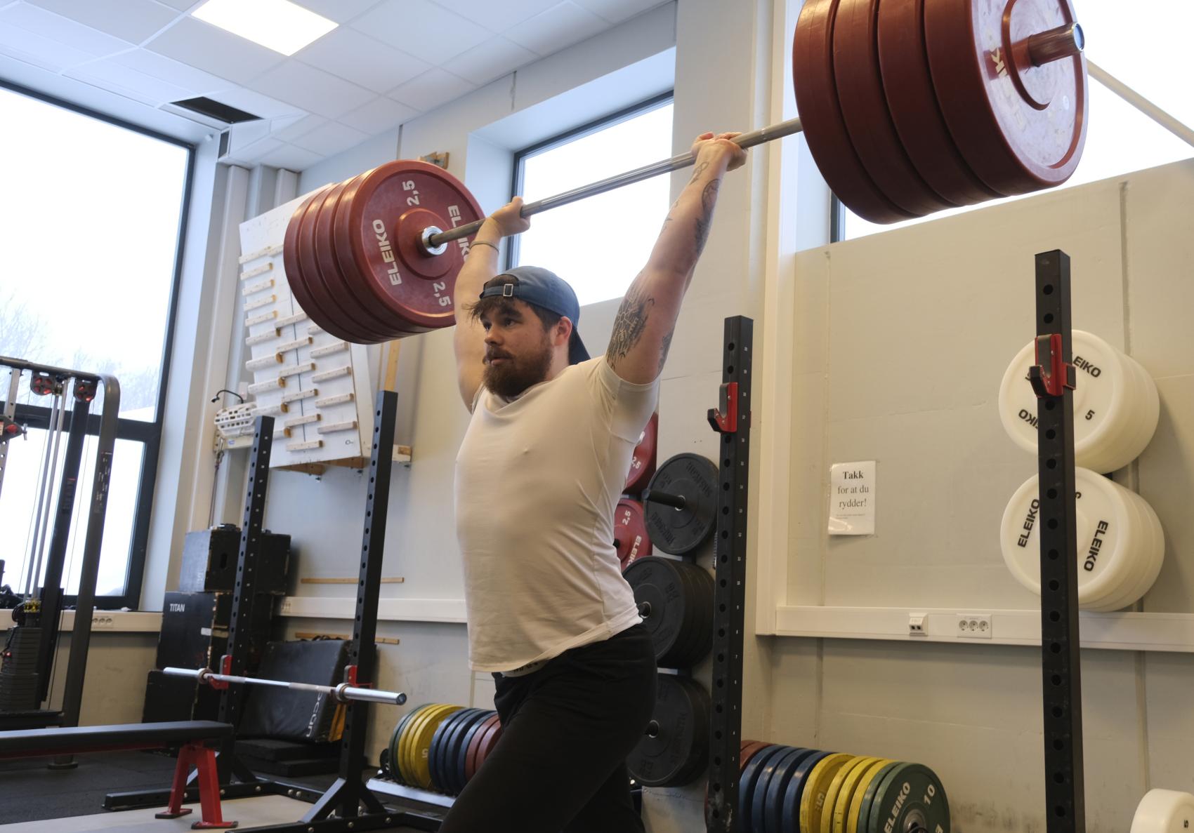 Ung mann med caps som løfter vekter over hodet. Foto